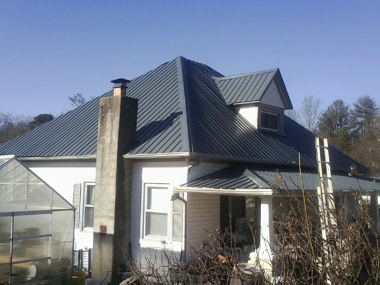 Dark blue standing seam metal roof on a white farmhouse with dormer — Slate & Tile Roof Repair by Roofing Brothers in Felda