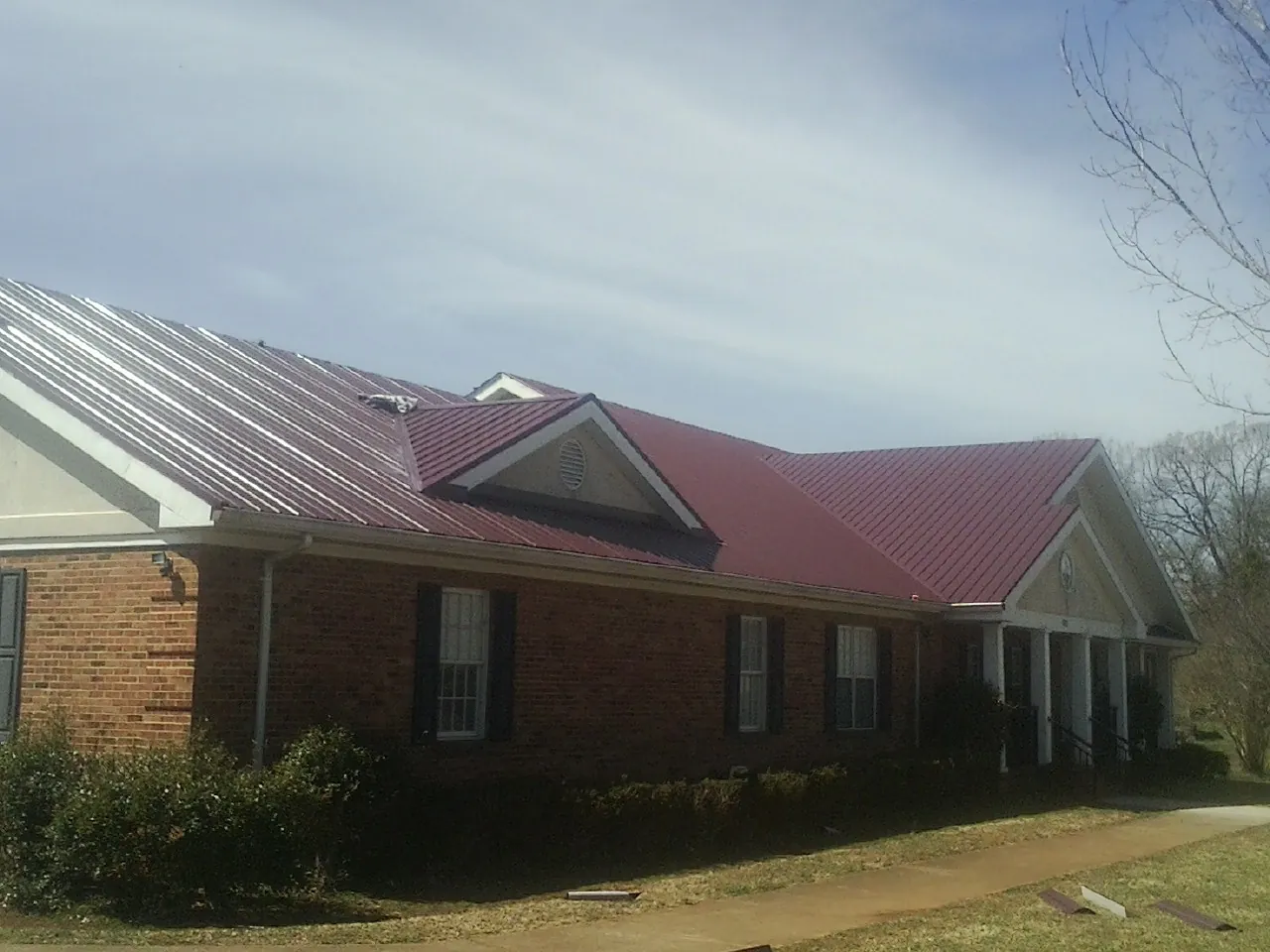 Red metal roof with gabled entries on a long brick building, from a Hail Damage Roof Repair job in Felda