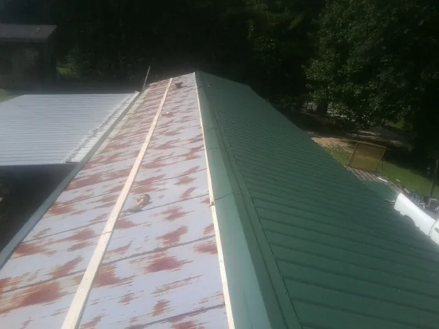 Old rusted panels beside newly installed green metal roofing — Wind Damage Roof Repair by Roofing Brothers in Felda