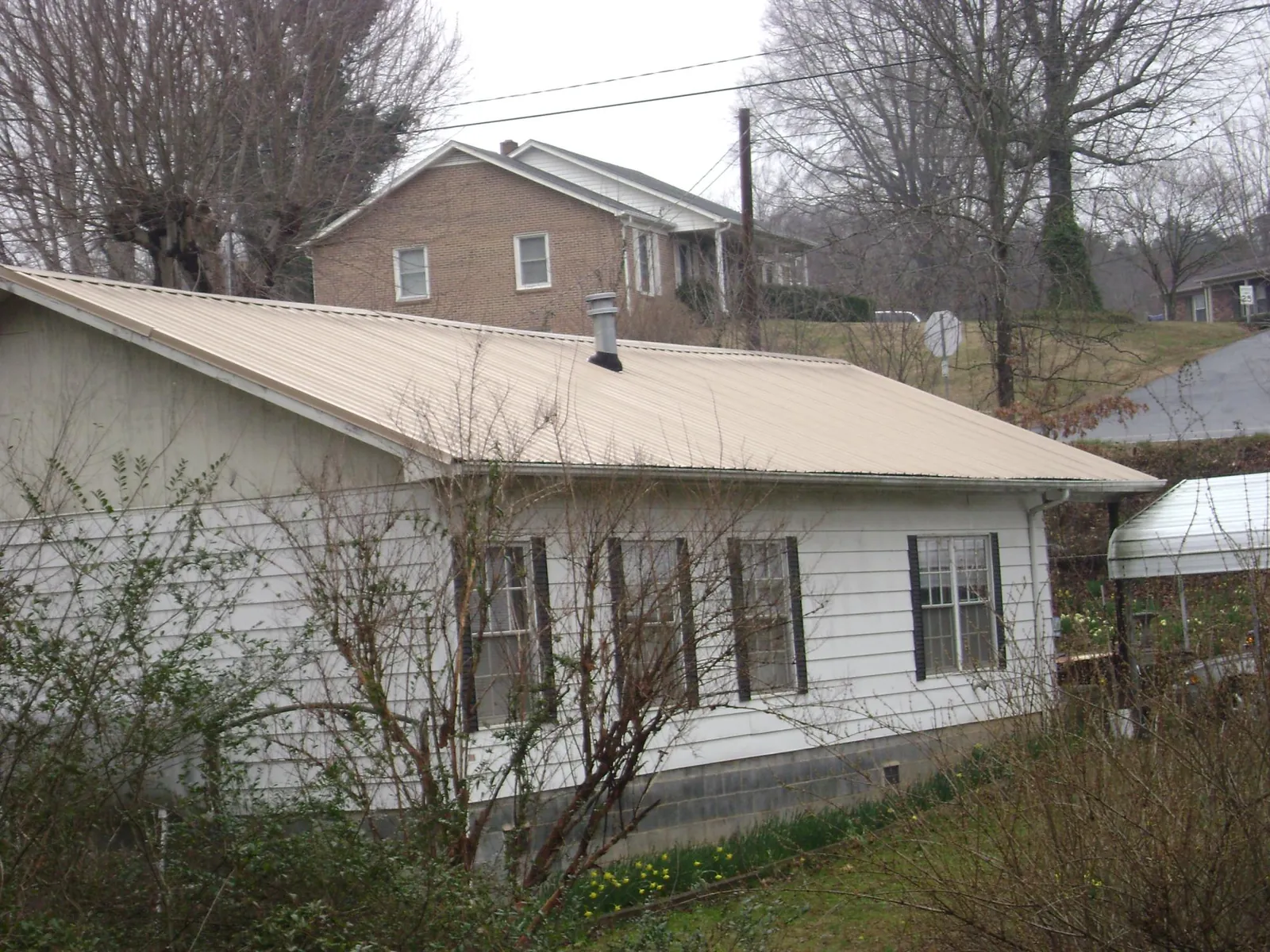 Tan metal roof on a white sided house set into a hillside — Commercial Roofing by Roofing Brothers in Felda